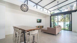 A modern dining area with a wooden table and white chairs, a beige sofa, and a TV mounted on the wall.