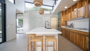 Una cocina moderna con una isla central, taburetes de madera y un gran ventanal que proporciona luz natural.