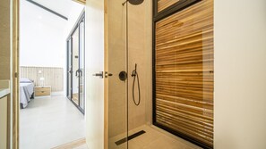 A modern bathroom with a glass shower enclosure, a wooden door, and a visible bathroom area with a bed and a nightstand. - Open Living Style Home 1Km From Beach (Potrero)