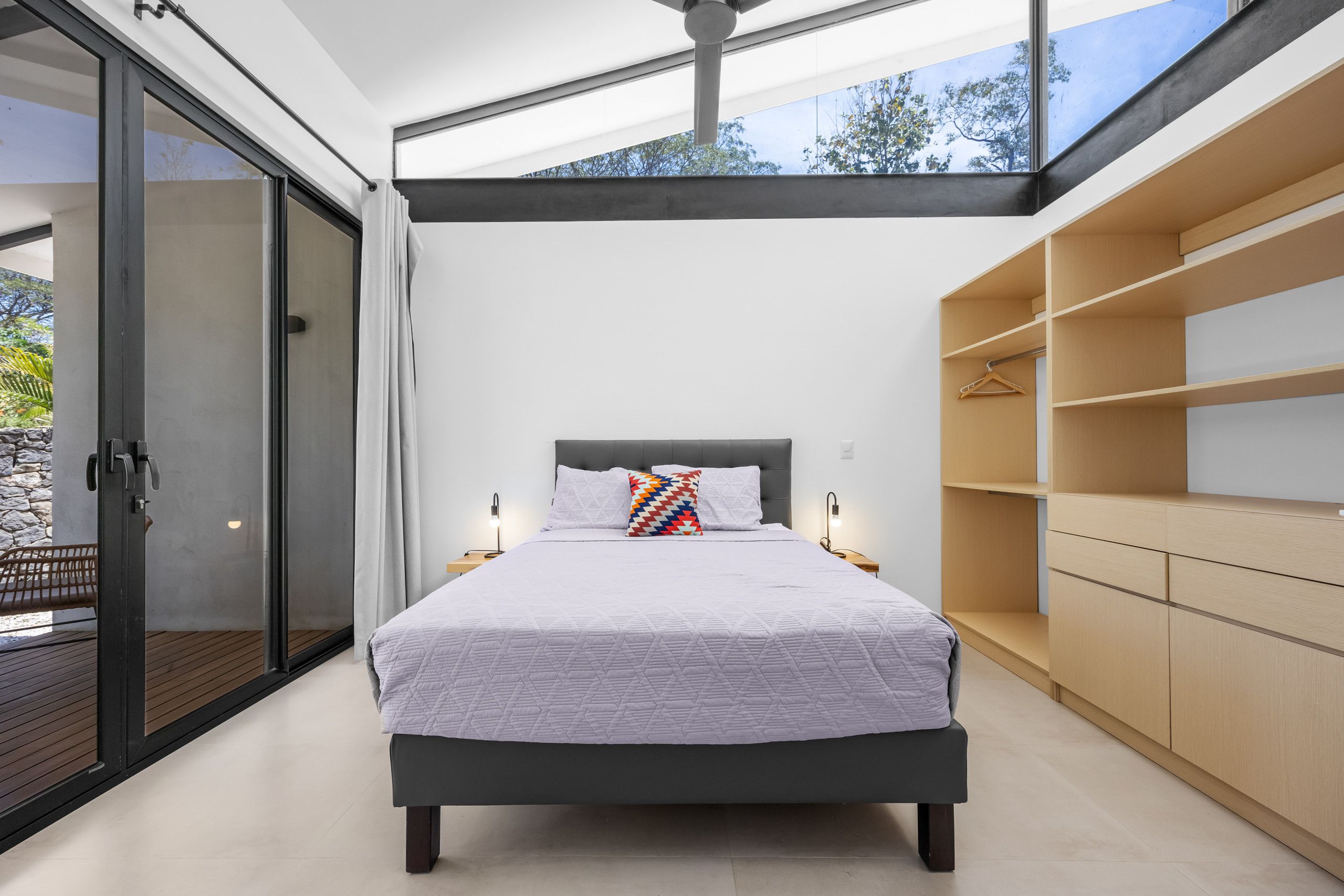 A modern bedroom with a large bed, a walk-in closet, and a glass door leading to an outdoor area.