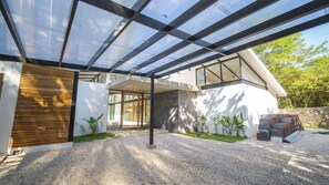A modern house with a covered patio area, a stone wall, and a gravel driveway. - Open Living Style Home 1Km From Beach (Potrero)