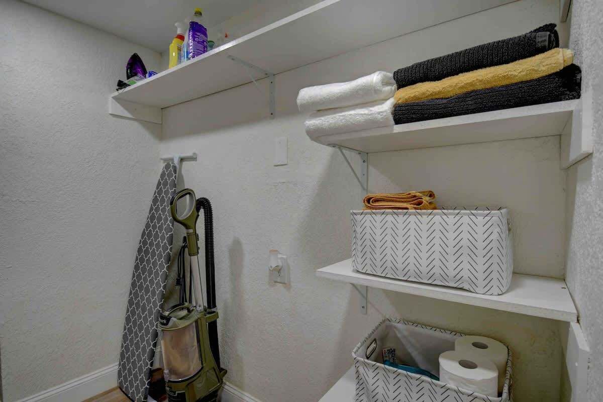 Um banheiro com porta-toalhas, prateleiras com toalhas, um aspirador de pó e cestos organizadores.