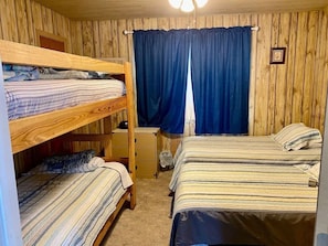 A room with bunk beds, a small desk, a chair, and a window with curtains.