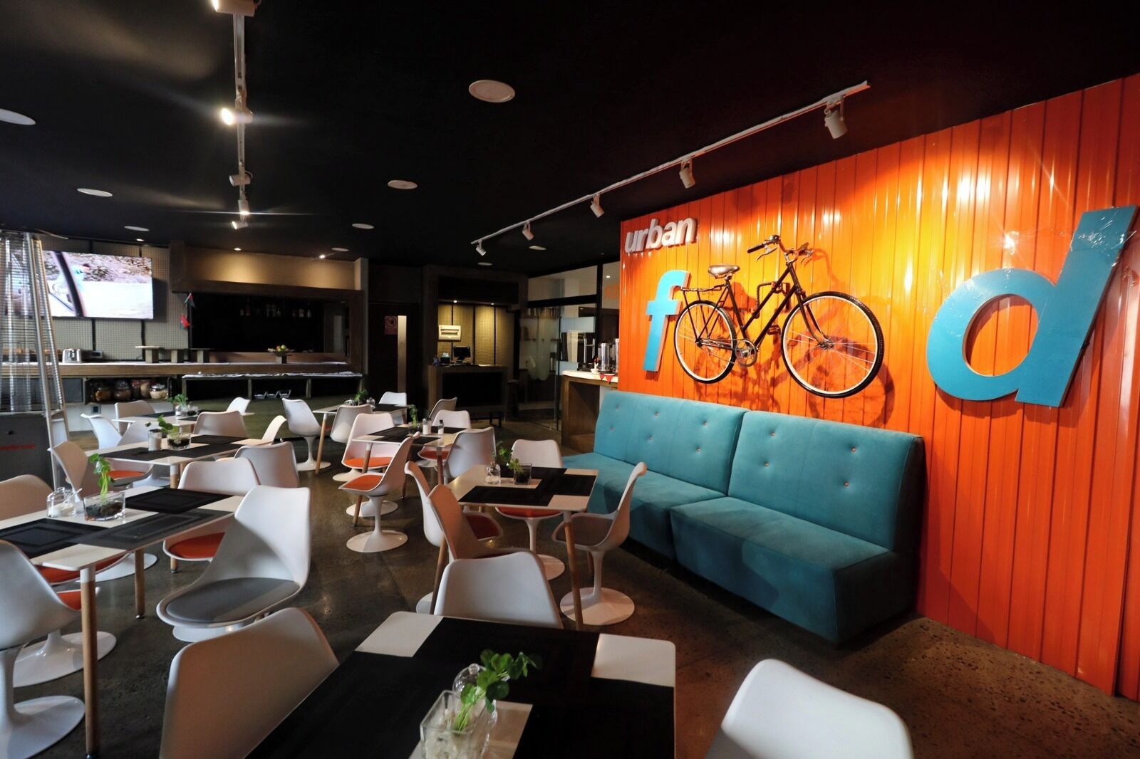 A modern restaurant with a blue sofa, white chairs, and tables. A large 'urban' sign with a bicycle is on the wall.