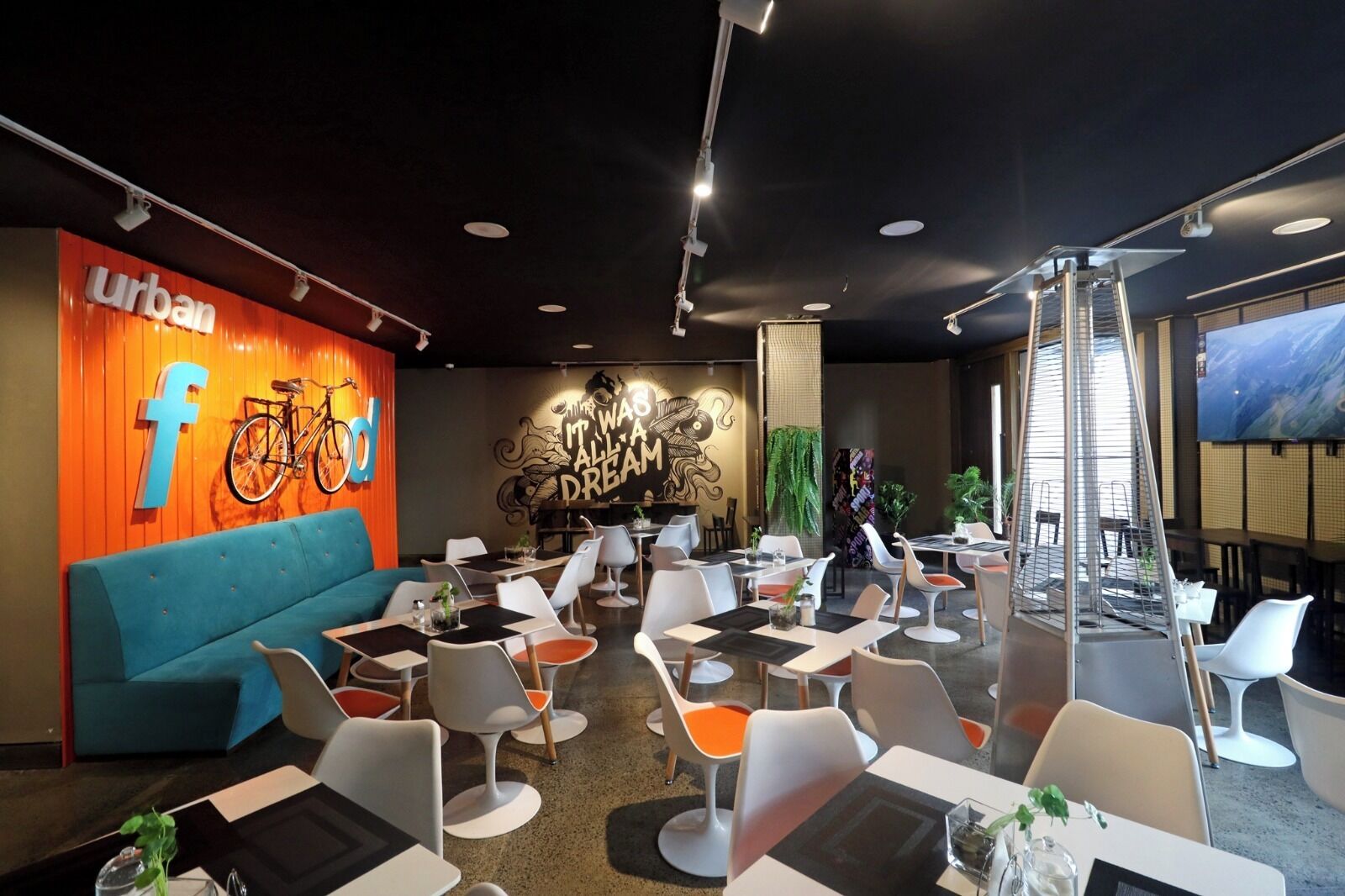Un comedor moderno con una variedad de estilos de asiento, incluyendo un sofá azul y diferentes sillas. Se ve un mural grande con una bicicleta y el texto 