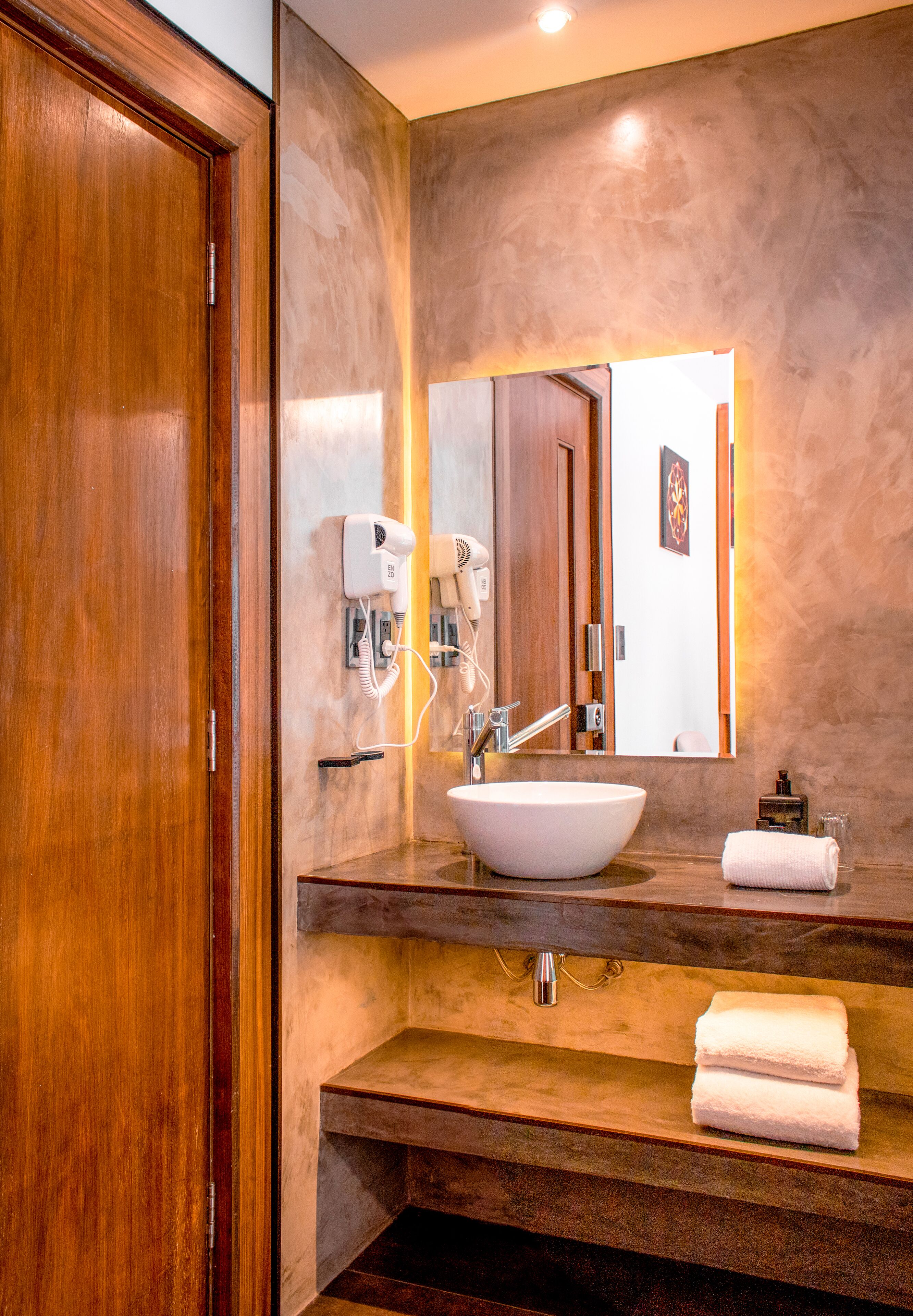 A modern bathroom with a wooden door, a large mirror, a white sink, and a towel rack.
