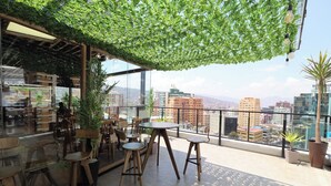 A rooftop terrace with wooden furniture, potted plants, and a view of the cityscape. - Madero Hotel & Suites (La Paz)