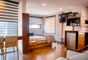 Una habitación pequeña con cama, escritorio y kitchenette.