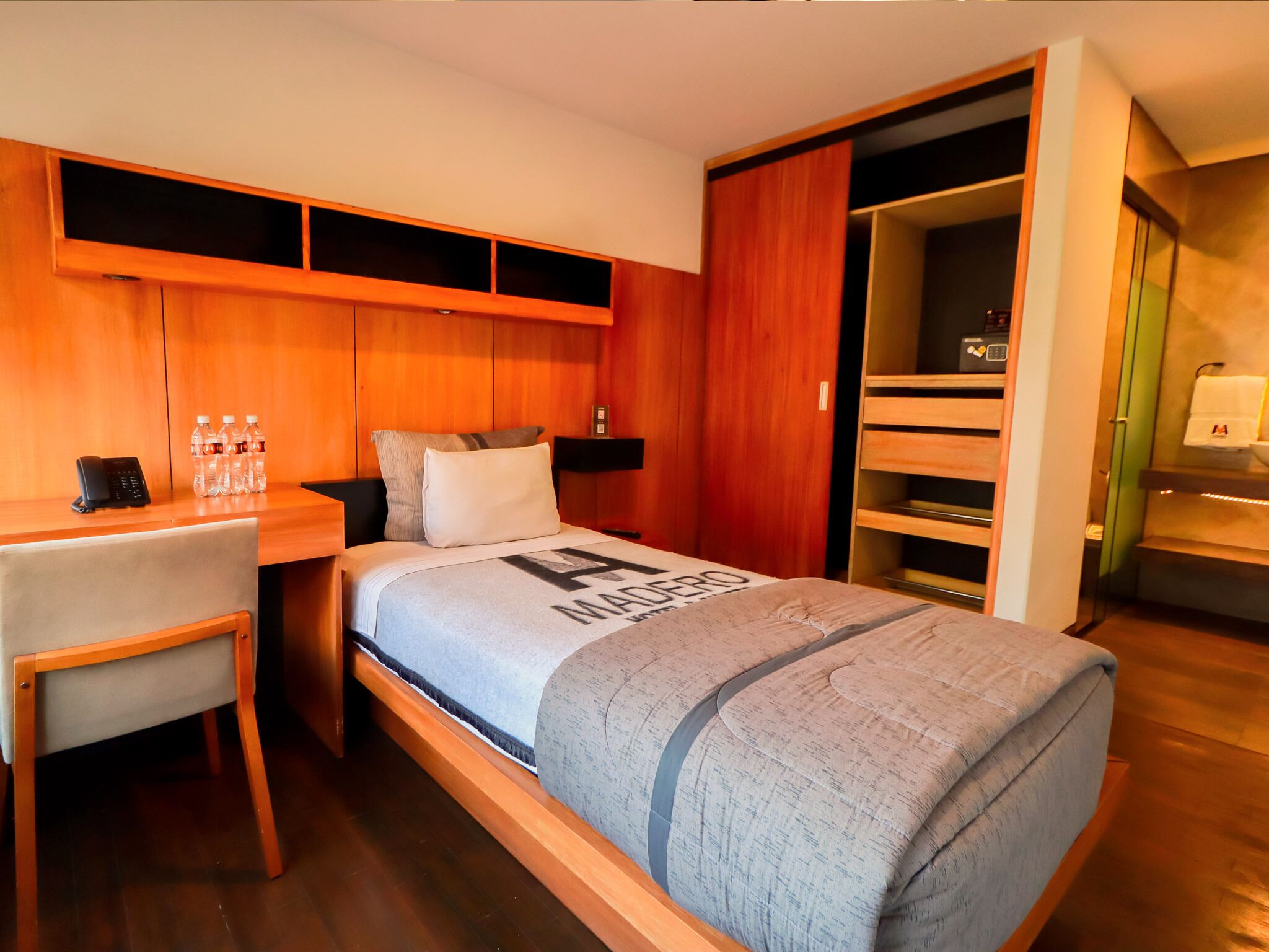 A hotel room with a bed, a desk with a phone and water bottles, a closet, and a bathroom.