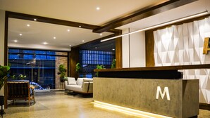 A modern reception area with a concrete reception desk, a sofa, and potted plants. - Madero Hotel & Suites (La Paz)
