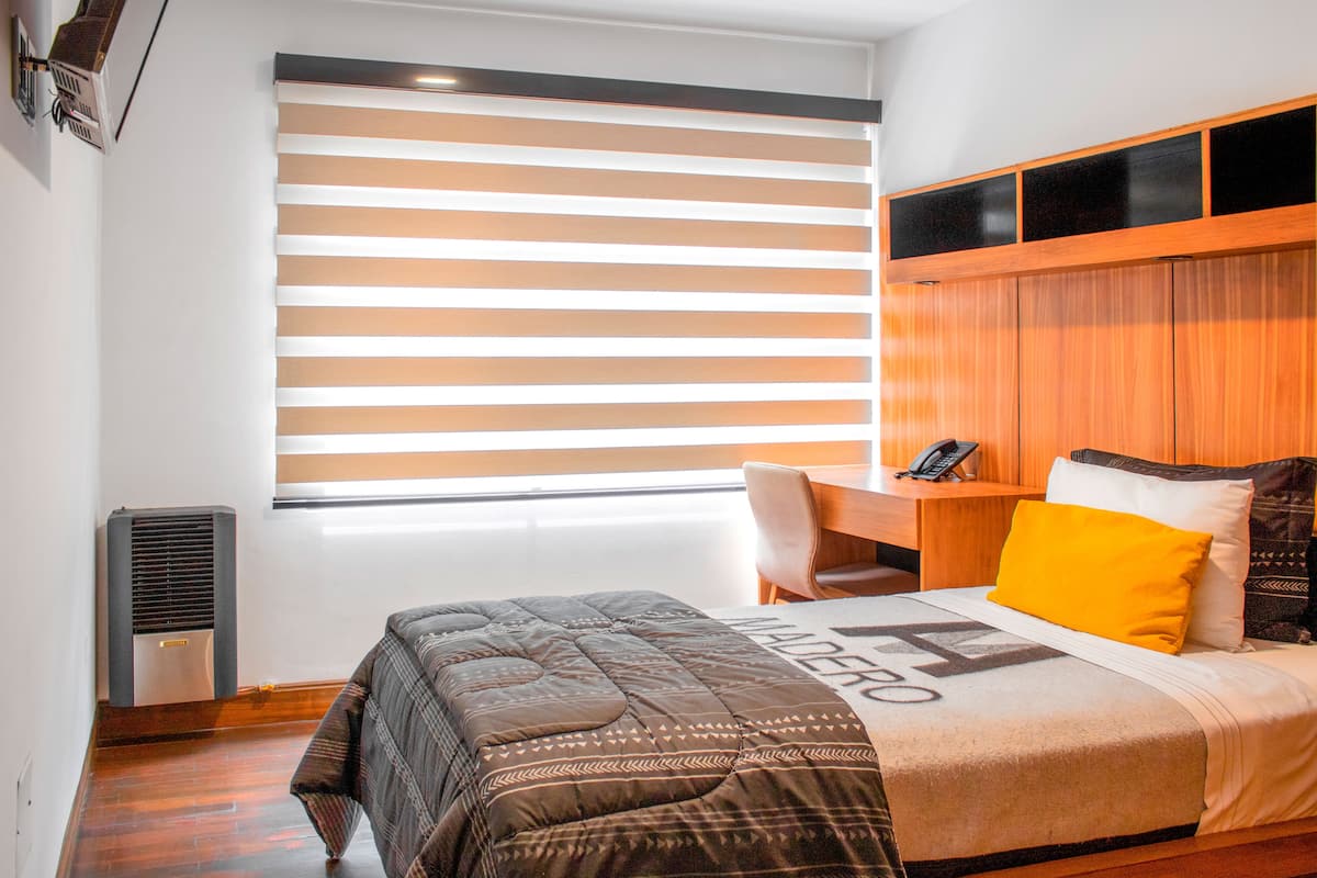 A bedroom with a bed, a desk, and a window with blinds.