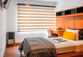 Un dormitorio con cama, escritorio y ventana con persianas.