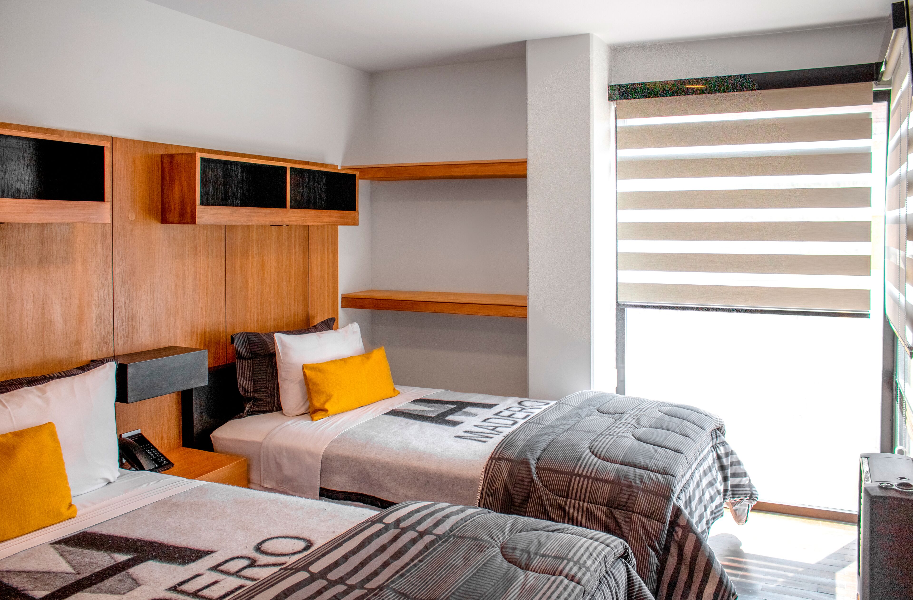 Ein modernes Hotelzimmer mit zwei Betten, Holz-Kopfteilen und integrierten Regalen.
