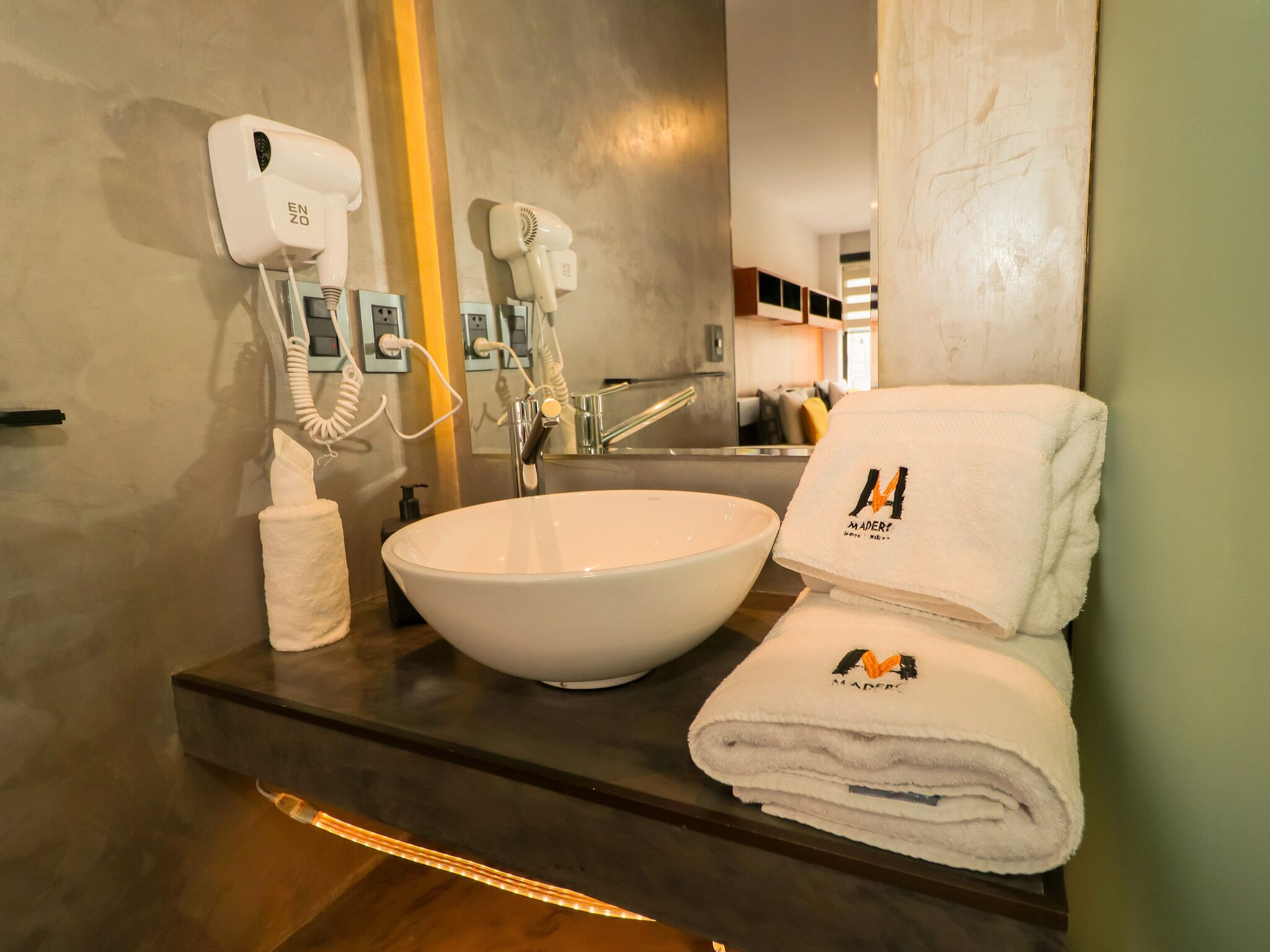 A modern bathroom with a large white sink, a hairdryer, and a towel with a logo.