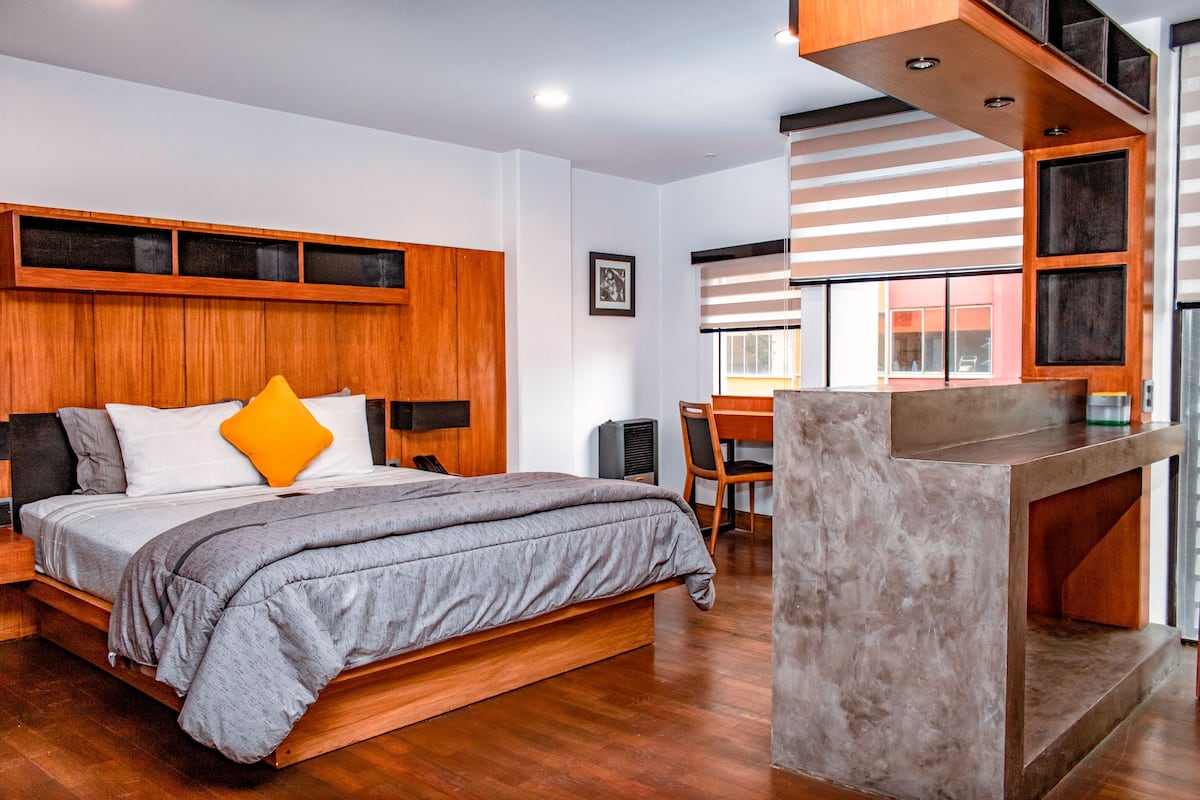 A modern bedroom with a wooden bed, a desk, and a staircase.