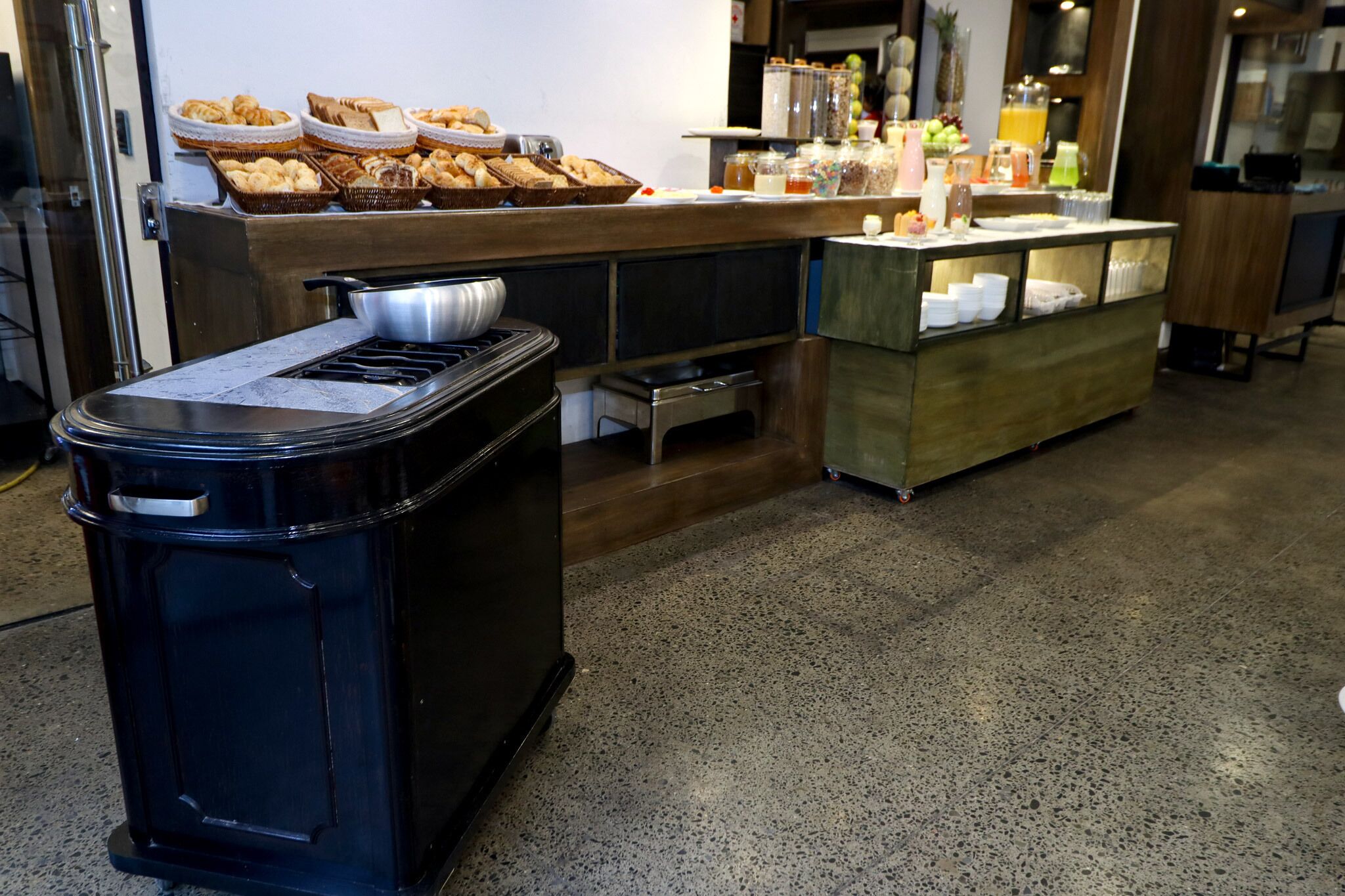 A kitchen area with a stove, a trash bin, and a buffet counter with various food items and beverages.