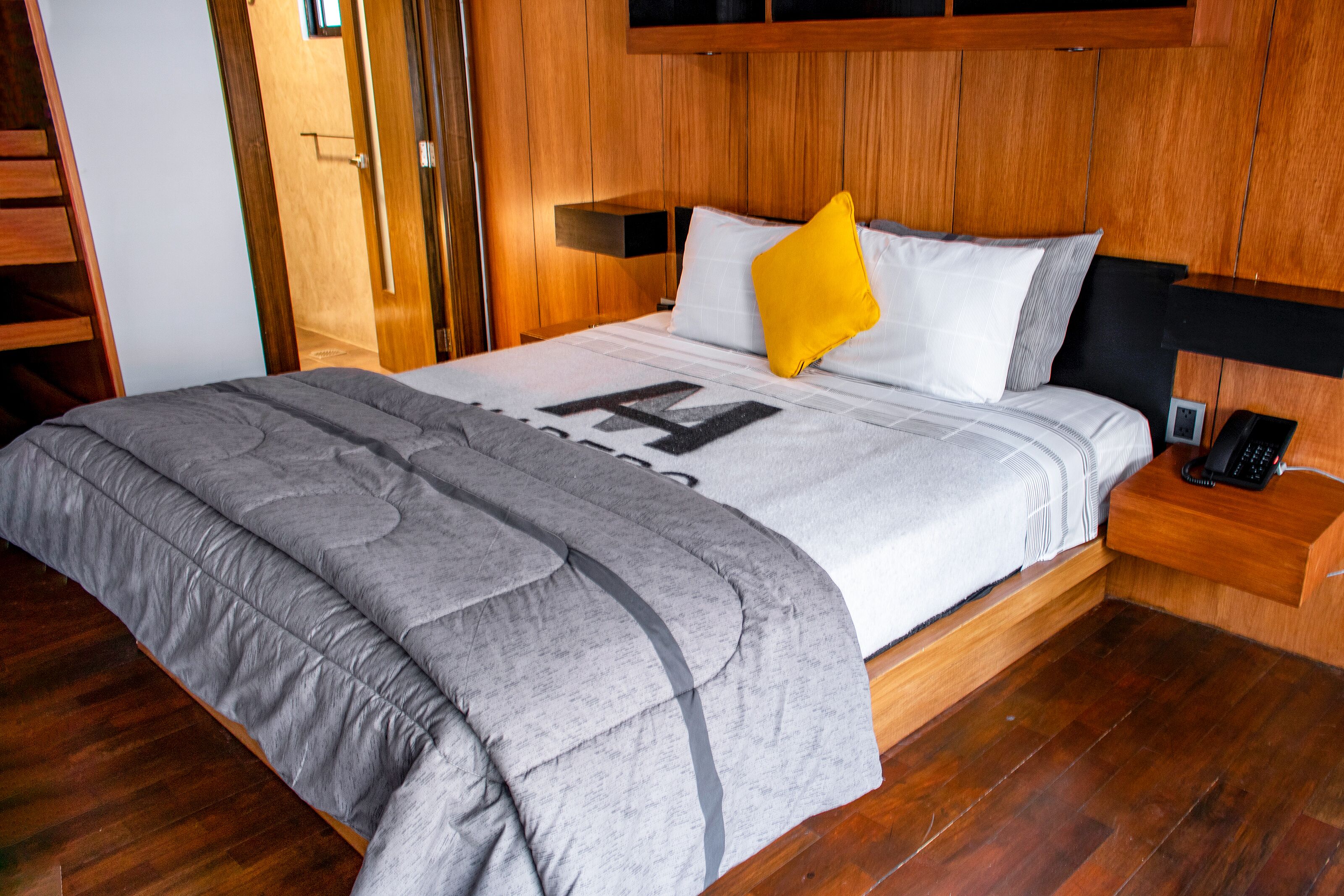 A neatly made bed with a grey and white duvet, a yellow pillow, and a black headboard.