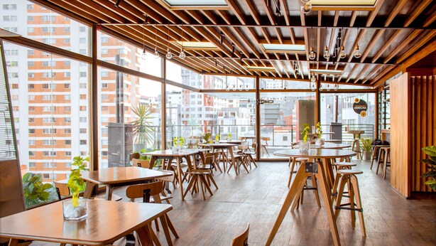 A modern restaurant with wooden tables and chairs, large windows with city views, and a wooden ceiling. - Madero Hotel & Suites (La Paz)