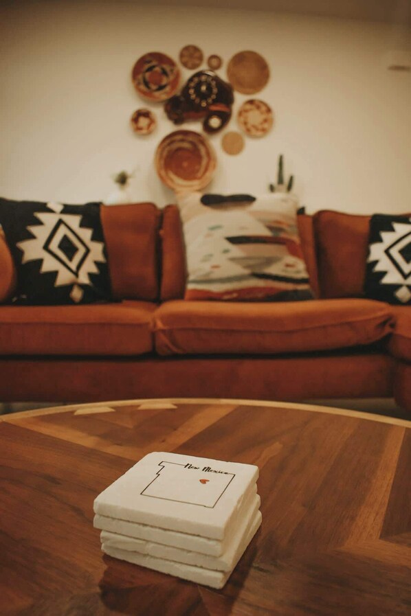 A living room with a wooden coffee table in the foreground and a sofa with patterned cushions in the background.