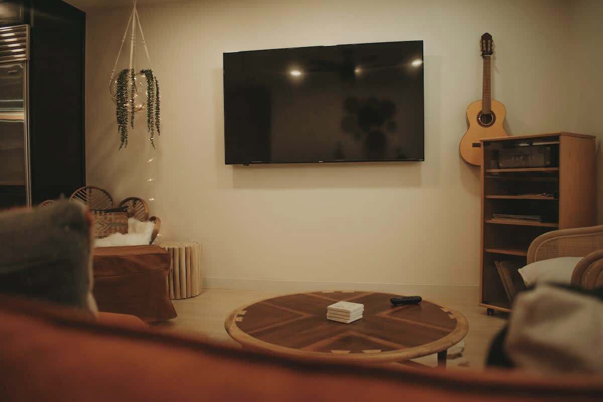 A living room with a flat-screen TV, a guitar, a bookshelf, and a round coffee table.