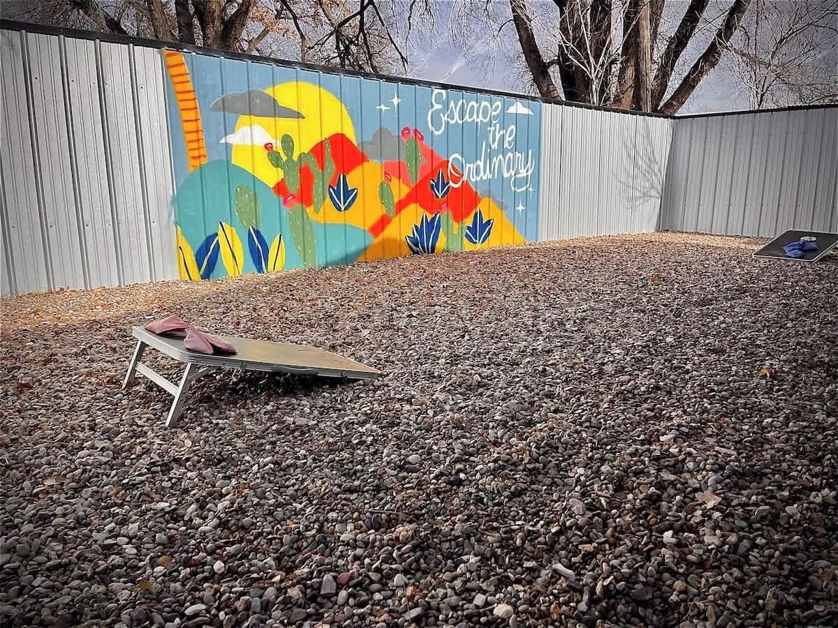 A gravel area with a metal bench and a colorful mural on a corrugated metal wall.