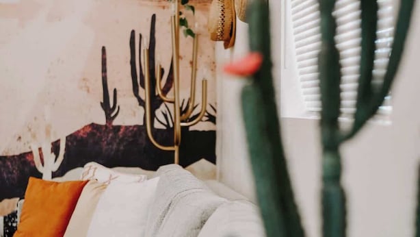 Een woonkamer met een bank, kussens, een cactus en een muur met een cactusmuurdecoratie.