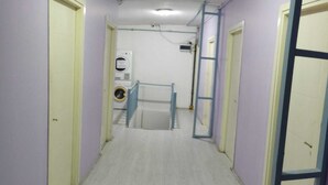 Un pasillo estrecho con paredes de colores claros y suelo de madera. Hay puertas a ambos lados y una lavadora en el centro.