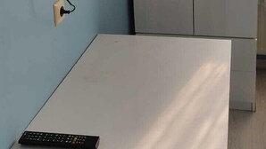 Una habitación con una televisión de pantalla plana montada en la pared, una mesita con un control remoto y un armario gris.