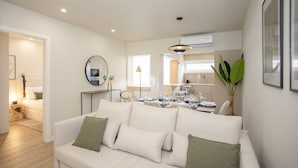 A modern living room with a sofa, a dining table set for four, and a kitchen in the background. - Liiiving in Porto-Uptown Pearl Apartment (Porto)