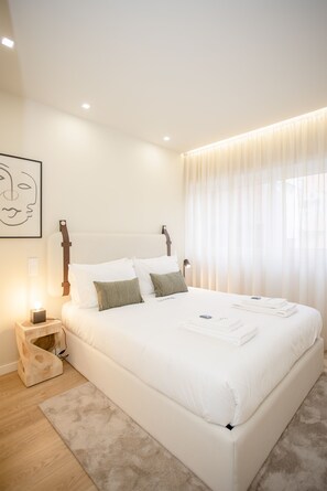 A neatly made bed with white linens, a bedside lamp, and a small wooden nightstand with a lamp. - Liiiving in Porto-Uptown Pearl Apartment (Porto)