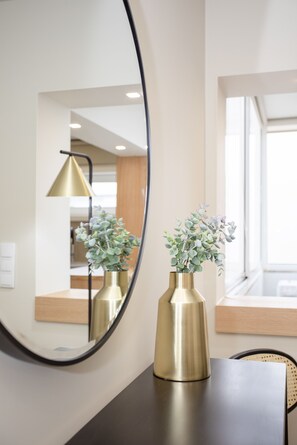 A mirror reflecting a room with a dark wooden table, two gold vases with green plants, and a gold floor lamp. - Liiiving in Porto-Uptown Pearl Apartment (Porto)