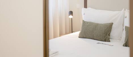 A neatly made bed with white linens, a headboard with a brown strap, and a bedside lamp.