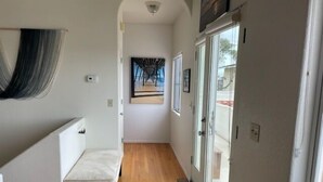 Un couloir étroit avec un banc, un tapis à motifs et une porte donnant sur un balcon.