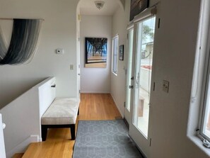 Un couloir étroit avec un banc, un tapis à motifs et une porte donnant sur un balcon.