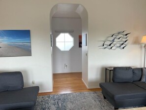 Un salon moderne avec deux canapés sombres, un tapis à motifs, une grande œuvre d’art abstraite accrochée au mur et un tableau représentant une scène de plage.