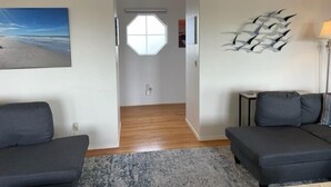 Un salon moderne avec deux canapés sombres, un tapis à motifs, une grande œuvre d’art abstraite accrochée au mur et un tableau représentant une scène de plage.