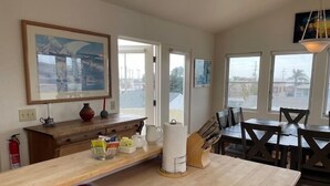 Une cuisine spacieuse dotée de plans de travail en bois, un coin repas avec une table et des chaises, et de grandes fenêtres offrant une vue sur l’extérieur.