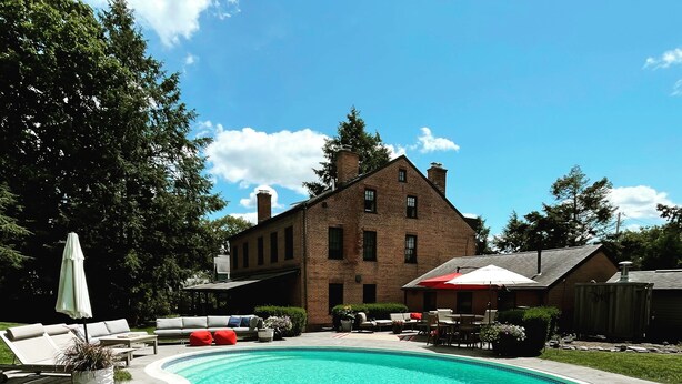 Une piscine avec un bâtiment en briques en arrière-plan, entourée d’herbe et d’arbres.