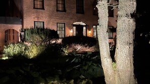 Un bâtiment en briques doté d’une entrée bien éclairée et d’un espace jardin agrémenté de plantes et d’un arbre.