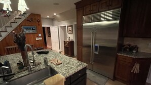 Une cuisine équipée d’un réfrigérateur en acier inoxydable, de plans de travail en granit, d’un évier encastré et d’armoires en bois.