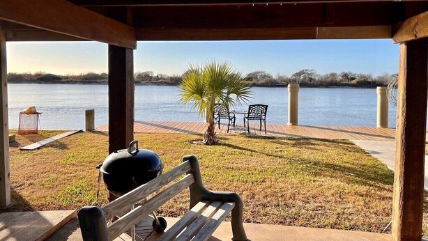 A covered outdoor area with a bench, a grill, and a view of a lake. - Waterfront Cabin with lighted fishing pier (Matagorda)