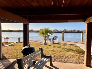 A covered outdoor area with a bench, a grill, and a view of a lake.