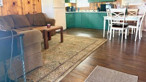A living room with a sofa, coffee table, and a dining area with a table and chairs. There is a kitchen with green cabinets and a refrigerator. - Waterfront Cabin with lighted fishing pier (Matagorda)