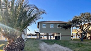A two-story building with a gravel driveway leading to a covered parking area. - Waterfront Cabin with lighted fishing pier (Matagorda)