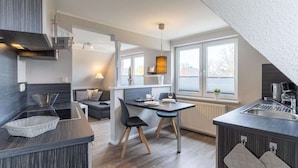 A modern kitchen with a dining area, large windows, and a built-in stove. - Ferienwohnung Dünenzauber (St.Peter Ording)