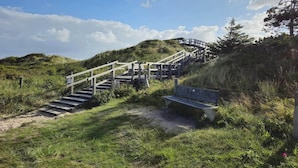 A wooden staircase leading up a grassy hill with a bench at the bottom. - Ferienwohnung Dünenzauber (St.Peter Ording)
