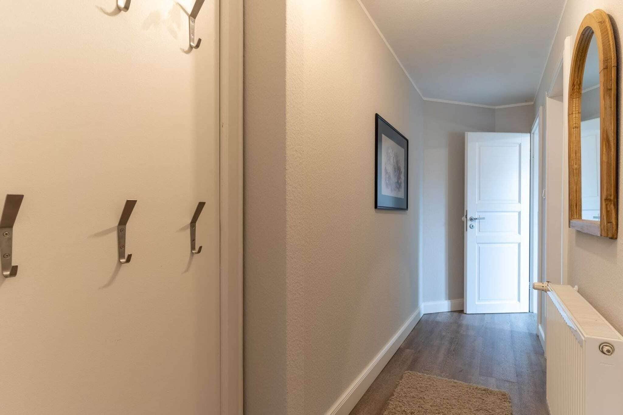Ein Flur mit einer weißen Tür am Ende, einem gerahmten Bild an der Wand und einem Heizkörper auf der rechten Seite.