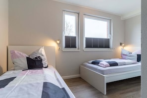 A bedroom with two beds, each with a headboard and pillows, and two windows with blinds.