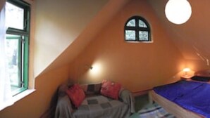 A bedroom with a sloped ceiling, a bed, a window, and a wall-mounted lamp.