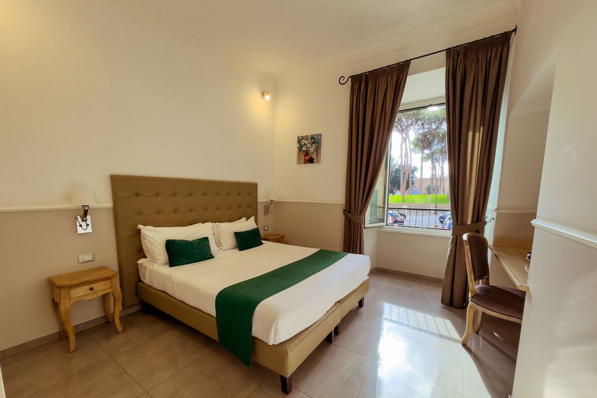 A hotel room with a large bed, a nightstand, a chair, and a view of the outside.